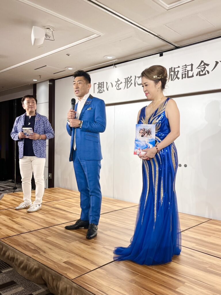 『想いを形に』出版記念パーティーでスピーチする谷島孝さんと、隣に立つ章予さん