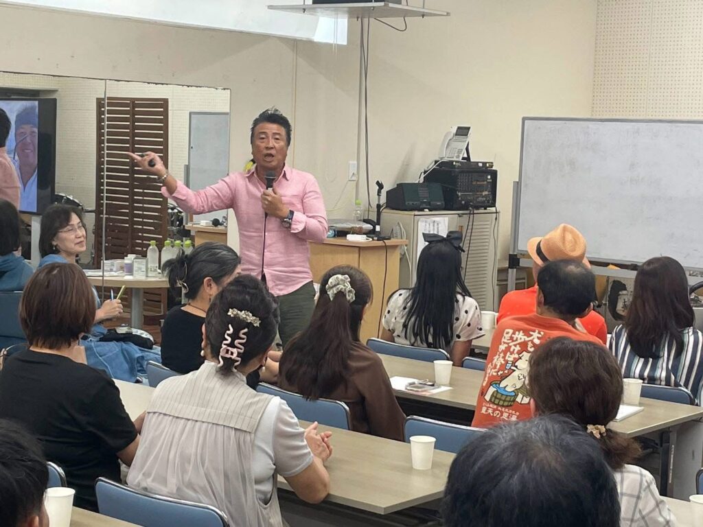 鹿児島県志布志市の講演会で、マイクを手に身振りを交えて語る辻幸一郎社長
