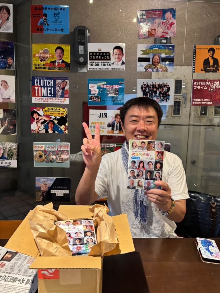 FM那覇のスタジオで『次世代伝承版2026秋号』を手にする平間正彦
